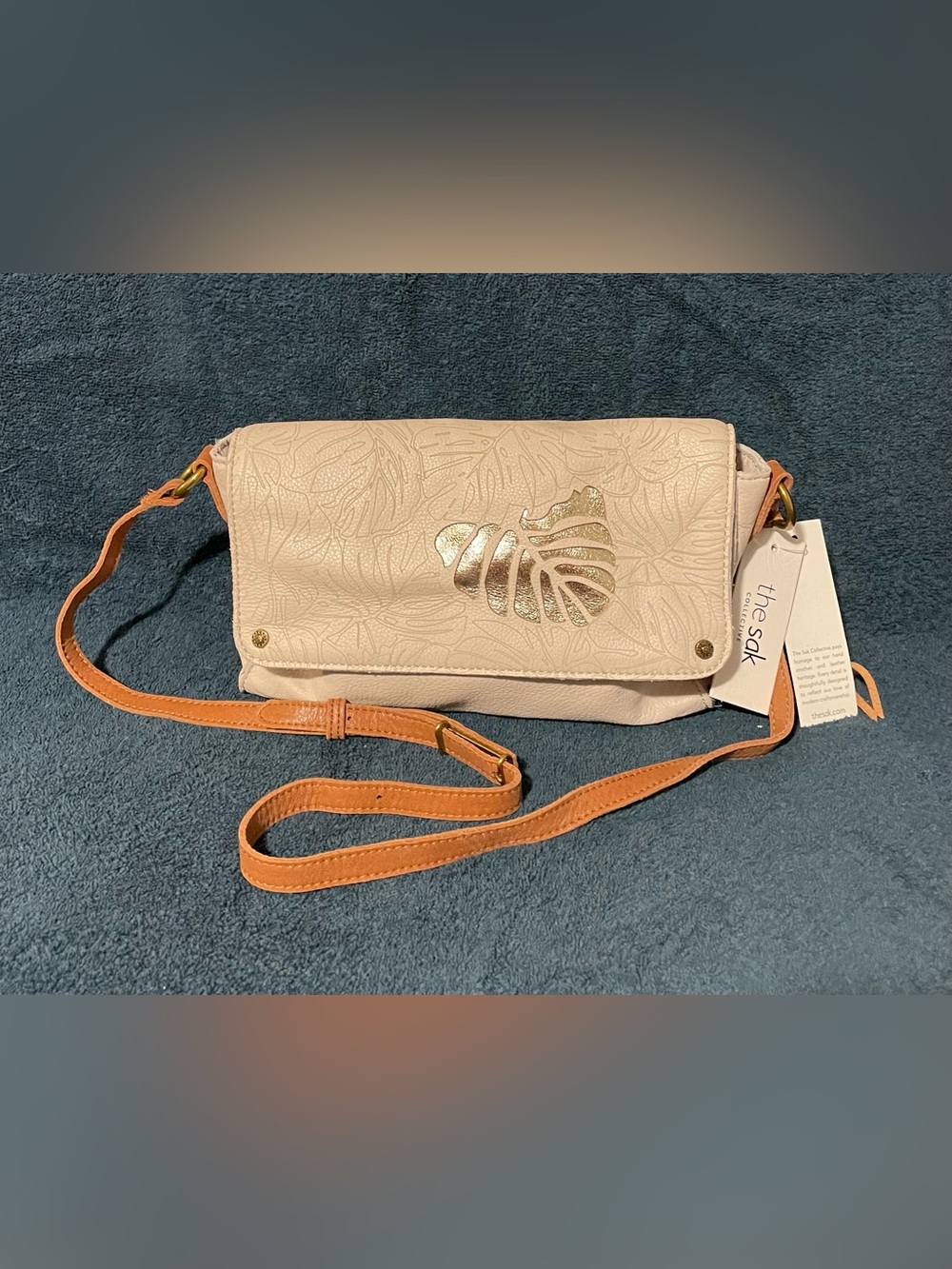 The Sak Cream Crossbody Bag with Tan Strap and Gold Leaf Accent